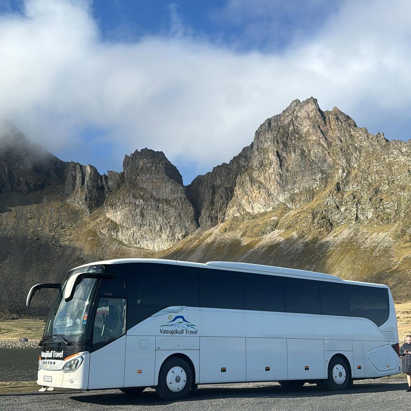 A Vatnajökull Travel coach parked beneath a jagged mountain ridge on the coast road