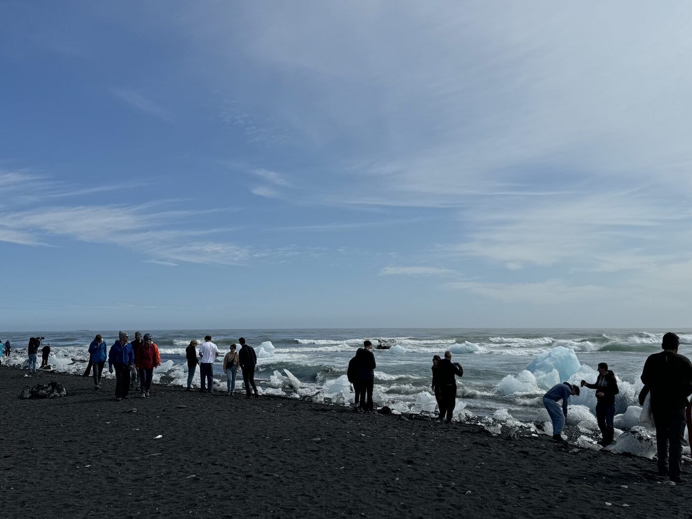 Visitors among blocks of glacier ice on the black sand of Diamond Beach