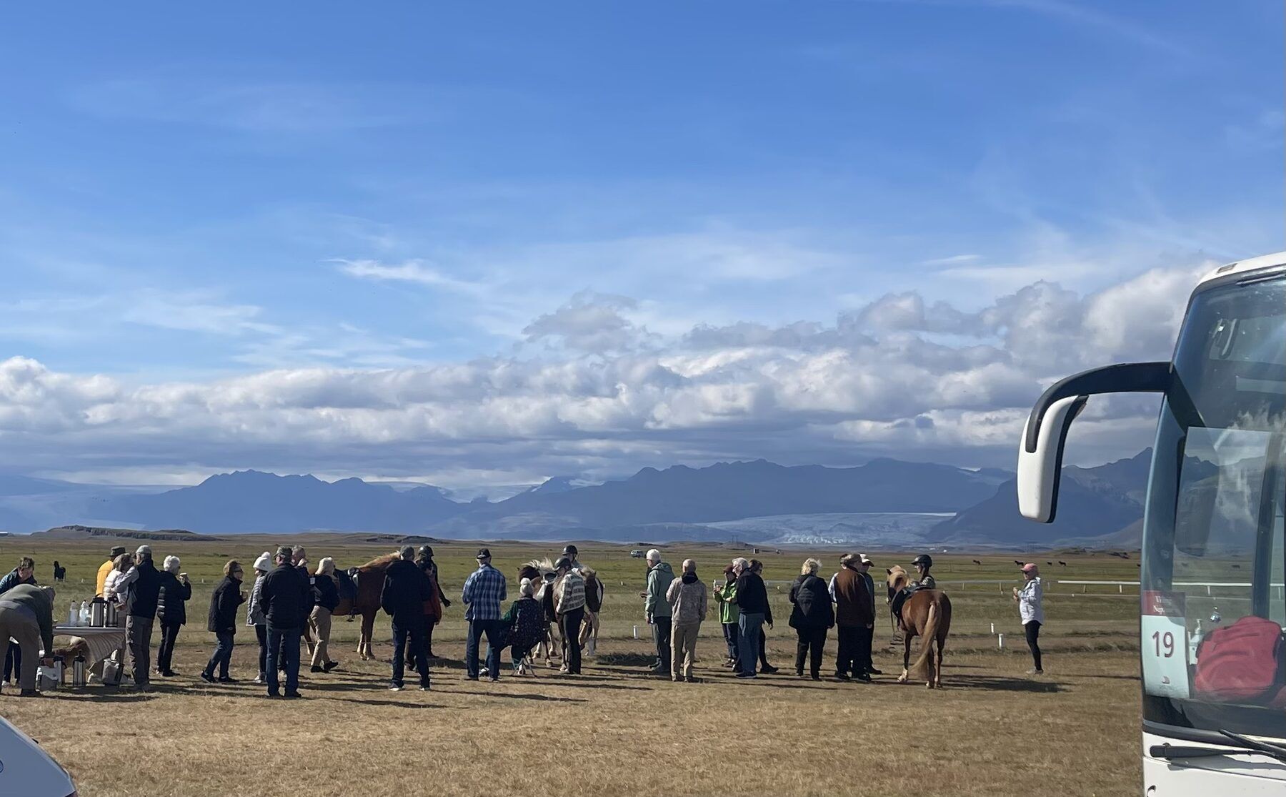 Guests and Icelandic horses in an open field beside a Vatnajökull Travel coach, the glacier on the horizon